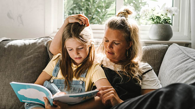 Mom and daughter reading book on sofa